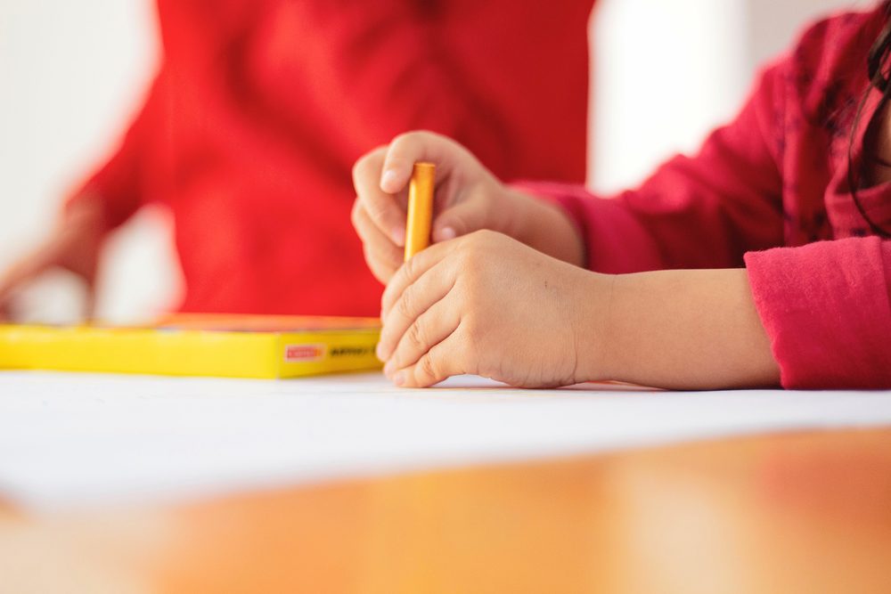 Kinderhand hält einen gelben Stift über einem Blatt Papier